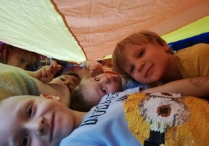 Dzieci leżą pod chusta animacyjną zaczepionej na małych krzesełkach w formie namiotu