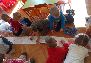 dzieci na papierze z długiej rolki wspólnie rysują " Świat dinozaurów". Praca odbywa się na podłodze