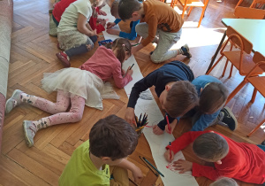 dzieci na papierze z długiej rolki wspólnie rysują " Świat dinozaurów". Praca odbywa się na podłodze