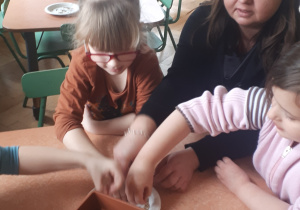 na zdjęciu dzieci wraz z nauczycielką sadzące owies do przygotowanych doniczek