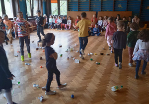 Na zdjęciu dzieci spacerują wśród porozrzucanych odpadów: plastikowych i papierowych.