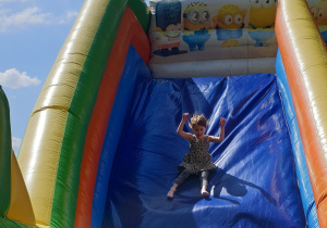 Na zdjęciu roześmiana dziewczynka zjeżdża z dmuchańca.