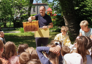 Na zdjęciu pszczelarz pokazuje wnętrze ula.