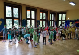 Na zdjęciu dzieci z papierowymi opaskami emblematem Żabek na głowach wesoło tańczące