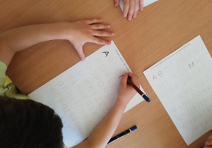 Na zdjęciu dzieci siedzą przy stolikach i tworzą prace plastyczne z kropek.