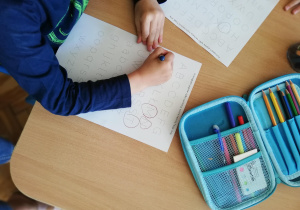Na zdjęciu dzieci siedzą przy stolikach i tworzą prace plastyczne z kropek.