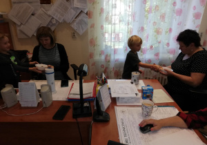 W gabinecie pań dyrektor - widać biurka, dwie panie dyrektor i dwoje dzieci podających paniom dyrektor miseczki z sałatką owocową