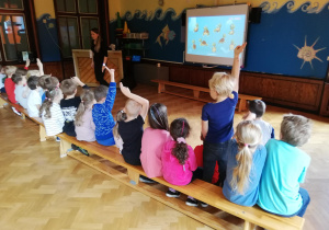 dzieci na sali przed tablica multimedialna, prowadzącą zajęcia objaśnia z pomocą projekcji na tablicy multimedialnej działanie japońskiego liczydła oraz zadaje dzieciom proste zagadki matematyczne