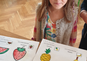 Zdjęcie przedstawia dziewczynkę z pokolorowanymi ilustracjami owoców