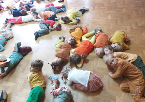 Dzieci w jesiennych kostiumach leżą na podłodze – zabawa „Magiczna liczba siedem