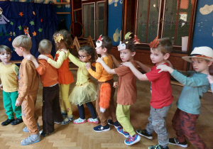 Dzieci w jesiennych kostiumach tańczą w wężyku