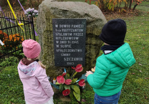 Dziewczynka i chłopiec stoją przy miejscu pamięci w którym spalono czterech partyzantów przez Hitlerowców w Słupie