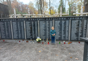 Dziewczynka zapala znicze pod pomnikiem Żołnierzy Armii Krajowej Batalionu „Zośka”