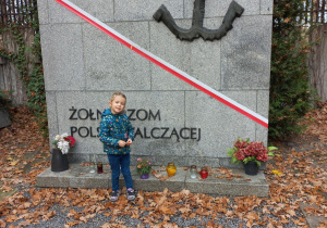 Dziewczynka zapala znicz pod pomnikiem dla „Żołnierzy Polski Walczącej”.