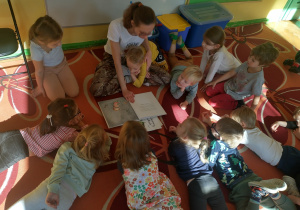 Dzieci leżą na dywanie w kole słuchając książki