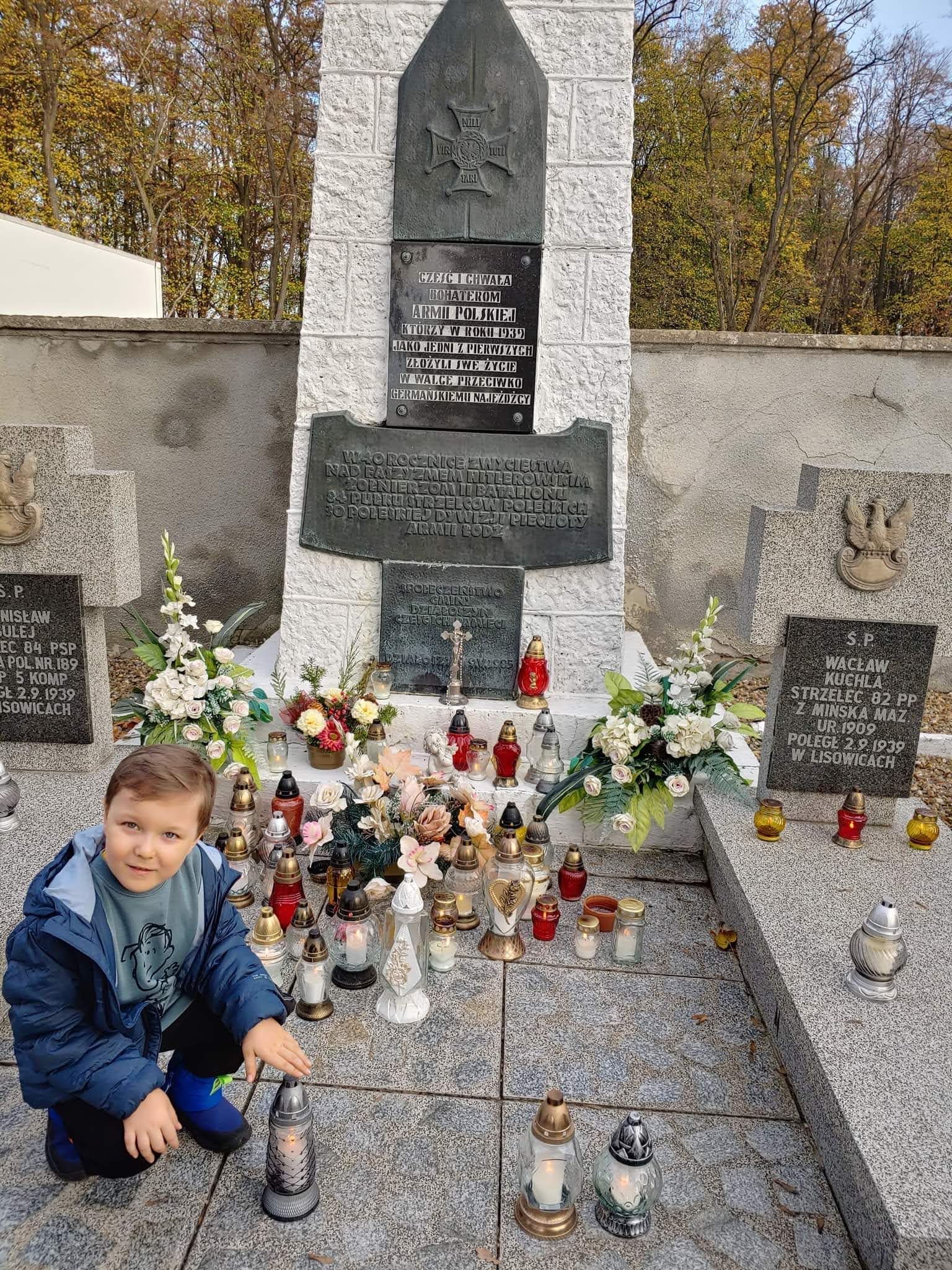 Na zdjęciu chłopiec, ze zniczem kucający przy grobie.