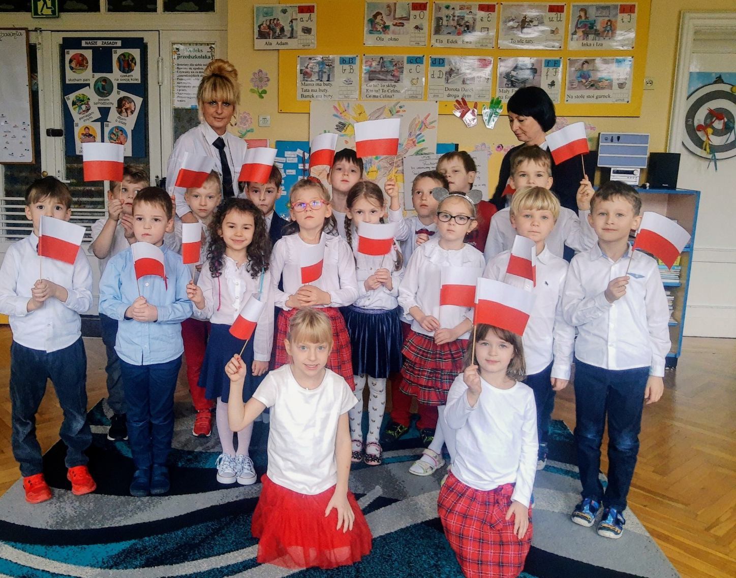 Na zdjęciu grupa Żabek wraz z nauczycielką w biało-czerwonych ubraniach z flagami Polski.