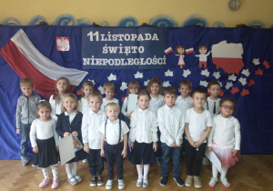 Dzieci z grupy trzeciej pozują do zdjęcia na tle dekoracji z okazji 11 listopada