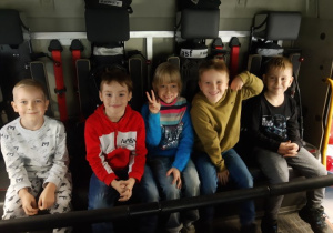 Uśmiechnięte dzieci przedszkolne pozują do zdjęcia siedząc w aucie strażackim.