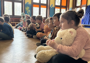 Na zdjęciu dzieci oglądające film edukacyjny przytulone do swoich misiów.