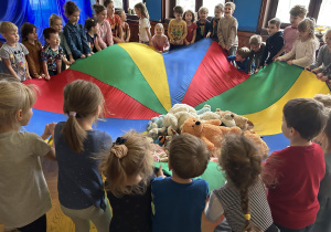 Na zdjęciu dzieci trzymają chustę animacyjną na której umieszczone są ich pluszowe misie.