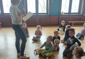 nauczycielka czyta zagadki siedzącym na podłodze dzieciom