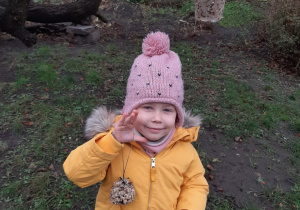 Na zdjęciu dziewczynka wiesza na drzewie pokarm dla ptaków.