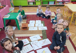 Na zdjęciu dzieci oglądają ilustracje ptaków odlatujących na zimę do ciepłych krajów i zostających w na zimę.