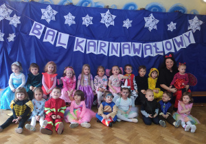 dzieci z grupy pierwszej wraz z nauczycielką pozują do zdjęcia grupowego na tle napisu "Bal Karnawałowy"
