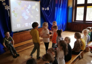 kilkoro dzieci stoi przed tablicą multimedialną, rozwiązują zadania na tablicy o tematyce dinozaurów