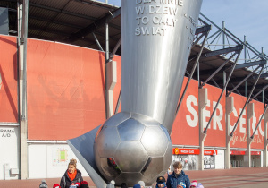 grupa dzieci stoi po wielkim pomnikiem twórców wielkiego Widzewa