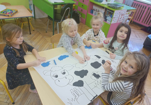 Dziewczynki wyklejają obrazek krowy plasteliną