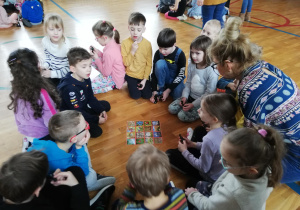 .dzieci siedzą w kole na podłodze i przyglądają się ilustracji z obrazkami o tematyce wiosennej