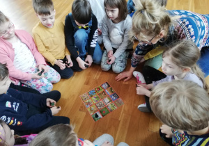 .dzieci siedzą w kole na podłodze i przyglądają się ilustracji z obrazkami o tematyce wiosennej