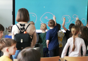 dzieci "piszą" palcami na tablicy multimedialnej