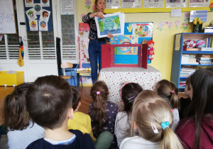 Nauczycielka pokazuje dzieciom ilustracje, elementy wykorzystywane do przedstawienia w teatrzyku Kamishibai