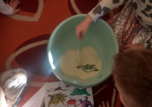 Dziewczynka odkrywa dinozaura schowanego w kaszy.