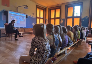 Na zdjęciu dzieci siedzące na ławkach słuchają pani adwokat czytającej książkę o Misiu Adwokacie.