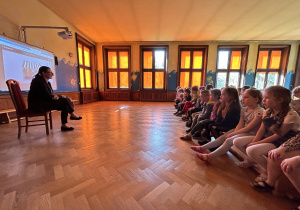 Na zdjęciu dzieci siedzące na ławkach słuchają pani adwokat czytającej książkę o Misiu Adwokacie.