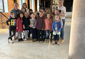 Na zdjęciu grupa dzieci z paniami odbijająca się w lustrze przed wejściem na spektakl.