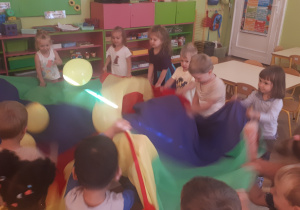 zdjęcie przedstawia dzieci z grupy ,,Misie” podczas zabawy z chustą animacyjną i balonami