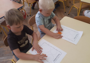 3-Zdjęcie przedstawia chłopców siedzących przy stoliku i wyklejających plasteliną