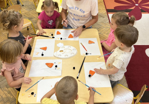 Na zdjęciu grupa dzieci wraz z nauczycielką wykonują przy stoliku pracę plastyczną.