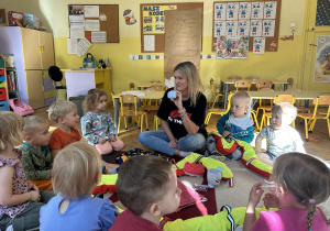 Na zdjęciu grupa dzieci wraz z nauczycielką bawią się na dywanie.
