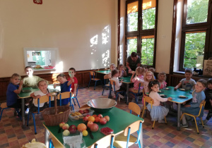 dzieci siedzą przy stolikach na jadalni, na stolikach przed każdym dzieckiem leżą talerzyki i plastikowe nożyki