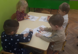 Na zdjęciu dzieci z grupy "Misie" siedzące przy stoliku i kolorujące obrazek dyni kredkami