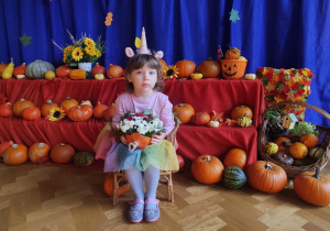 Dziewczynka siedząca na krześle na tle dyń