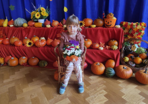Dziewczynka siedząca na krześle na tle dyń