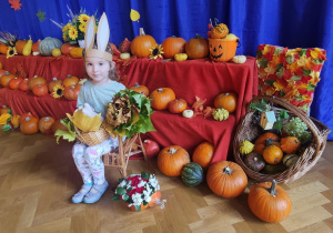 Dziewczynka w przebrani zajączka siedząca na krześle na tle dyń