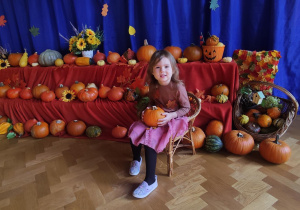 Dziewczynka pozująca na tle jesiennej dekoracji z dyń